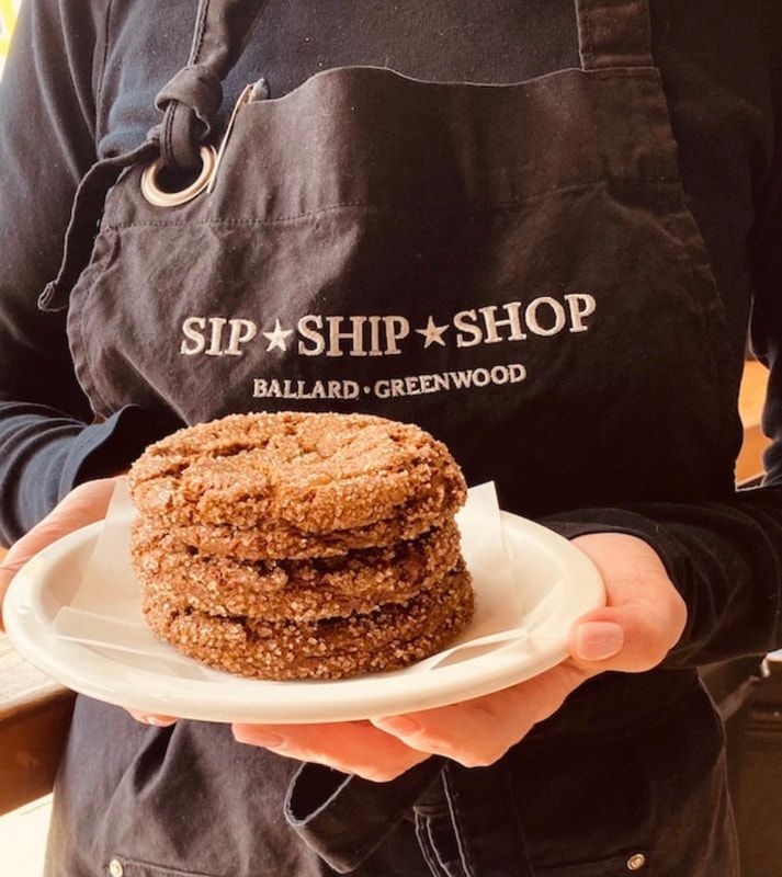Person holding a plate with a stack of cinnamon-sugar pastries, wearing a Sip & Ship Shop apron.