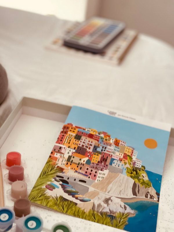 Paint-by-numbers canvas of colorful seaside houses, with paints and supplies in the foreground
