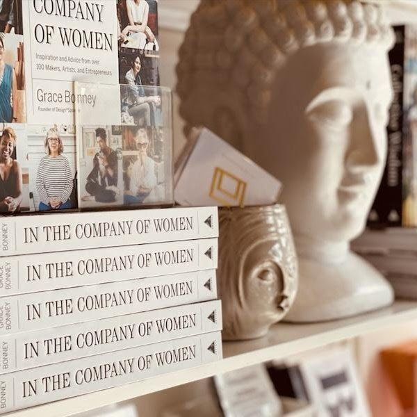 Stack of books beside a white Buddha head sculpture and framed photos on a shelf