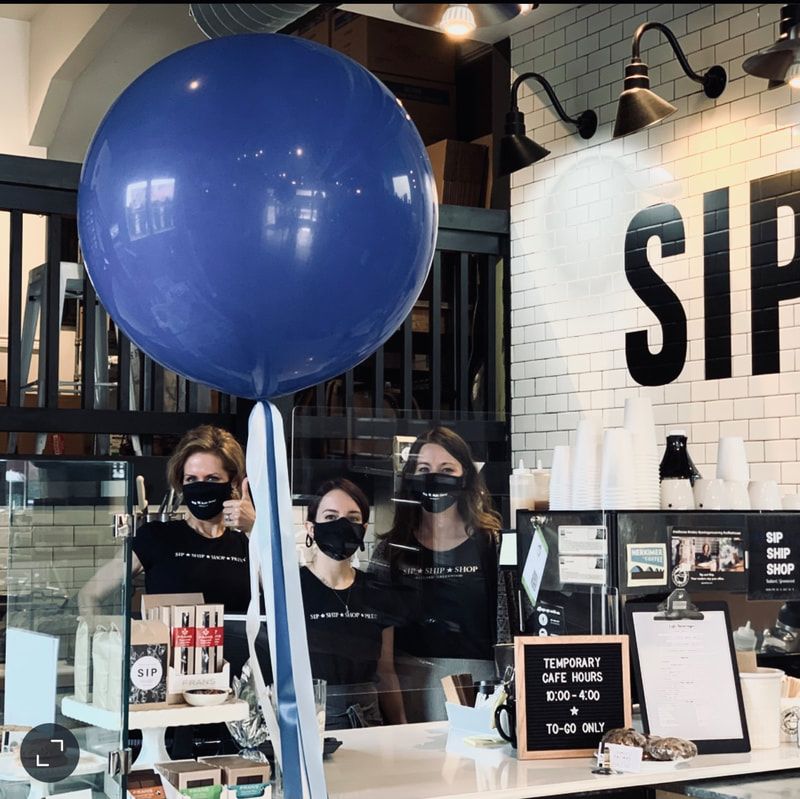 Staff behind a café counter holding a large blue balloon in a modern shop interior