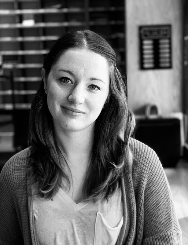 Woman with long hair smiling in a softly lit indoor setting, wearing a cardigan over a light shirt.
