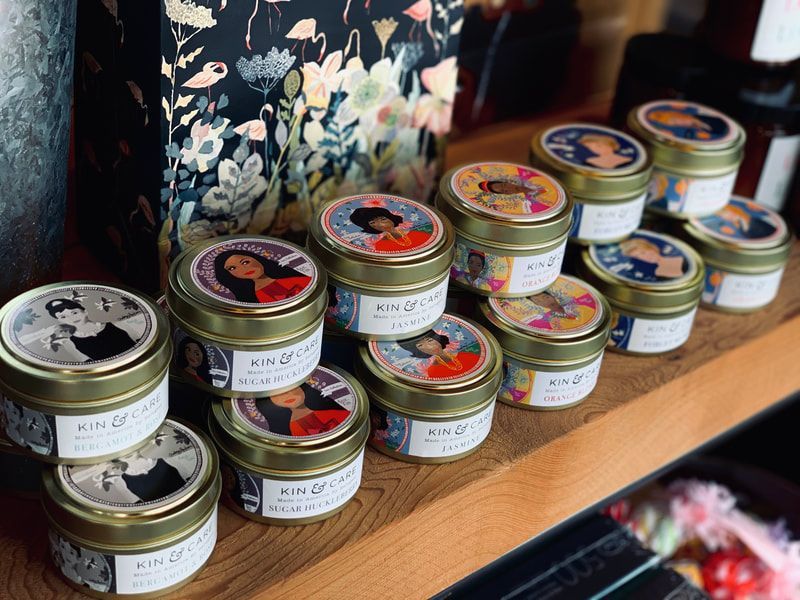 Small jars of cream or balm with colorful lids arranged on a wooden shelf beside floral fabric.