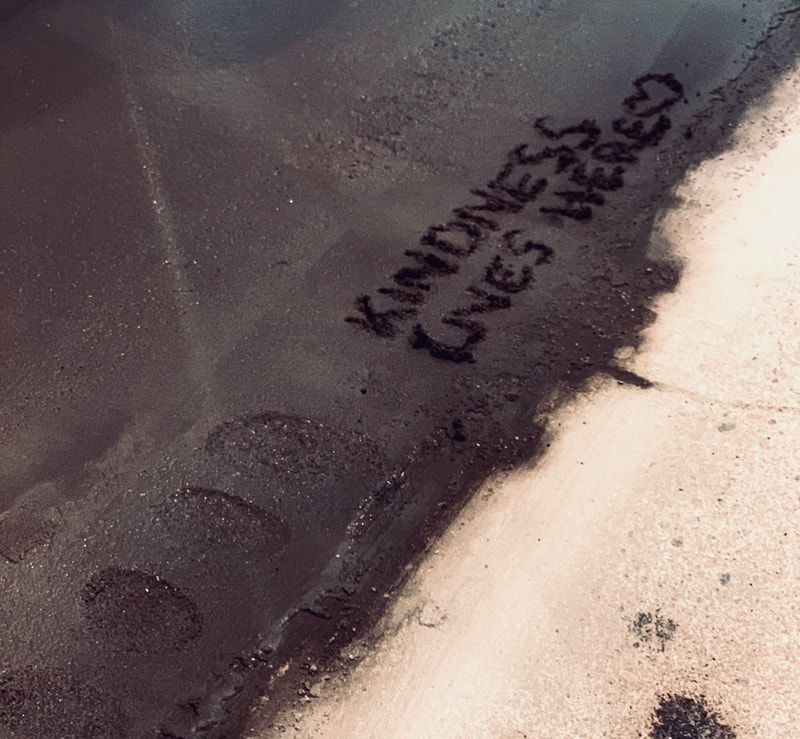 Close-up of a dark pavement edge beside pale sand, with black spray-painted text on the surface.