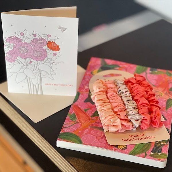 Greeting card and floral gift packaging on a table, with pink flower designs and folded card open.