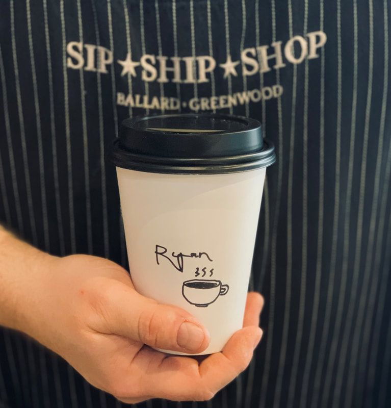 Hand holding a white takeaway coffee cup with a black lid, in front of a striped Sip Ship Shop apron.