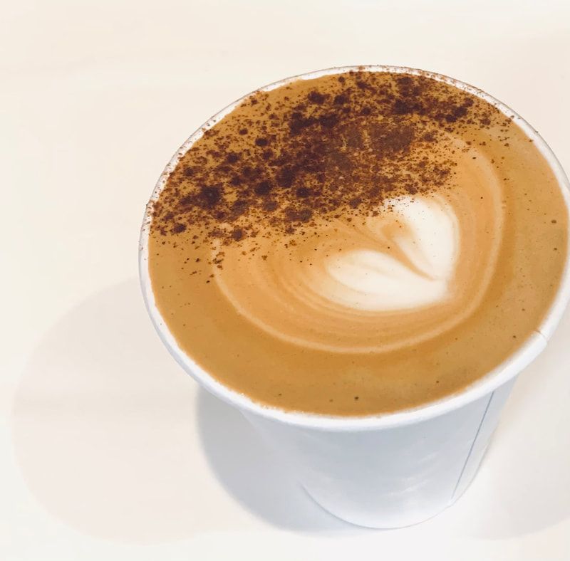 Cup of coffee with cocoa powder and latte art on a white table.