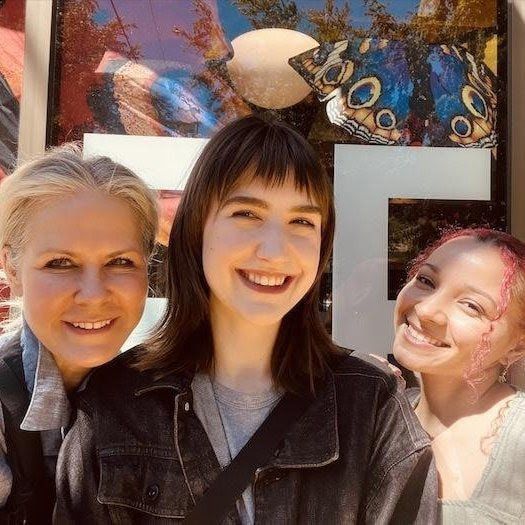 Three smiling people posing outdoors in front of a colorful wall mural