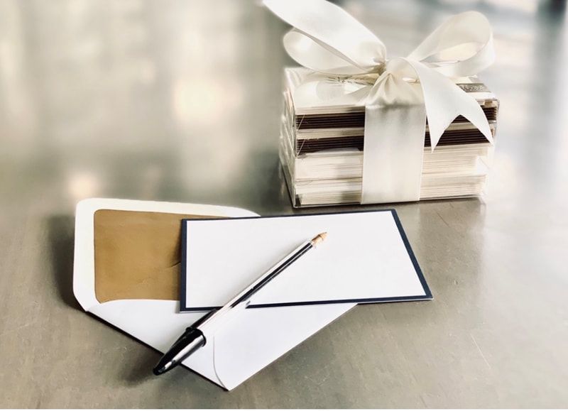 Wrapped gift with white ribbon beside open envelope, card, and pen on a reflective surface
