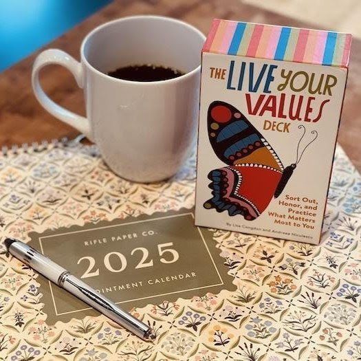 Coffee mug, 2025 planner, pen, and “Live Your Values” deck on a patterned tablecloth.