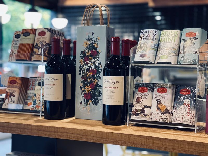 Gift display with wine bottles, floral bags, and assorted packaged goods on a wooden shelf.
