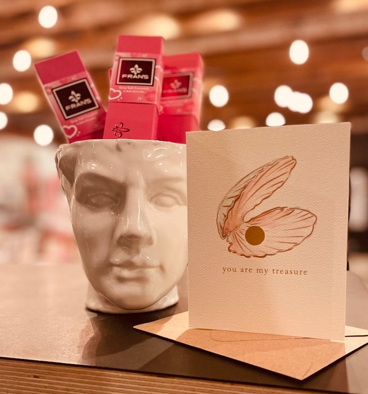 White face vase holding pink packets beside a cream card with a feather design on a warmly lit table