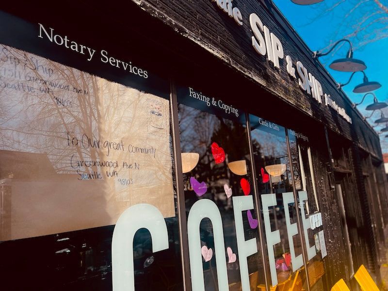 Storefront with a blue awning and large COFFEE sign, showing notary services and a window display of hats.