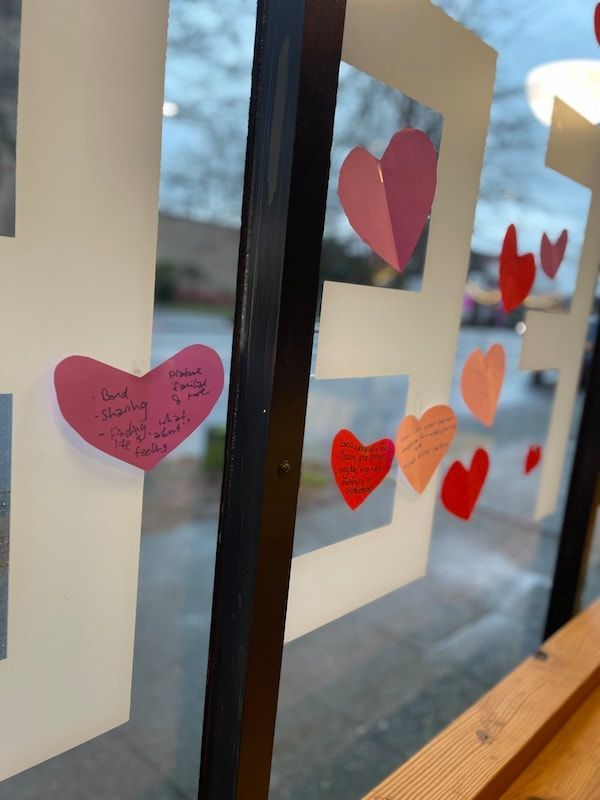 Heart-shaped notes on a window, with colorful hearts and reflections of the sky outside.