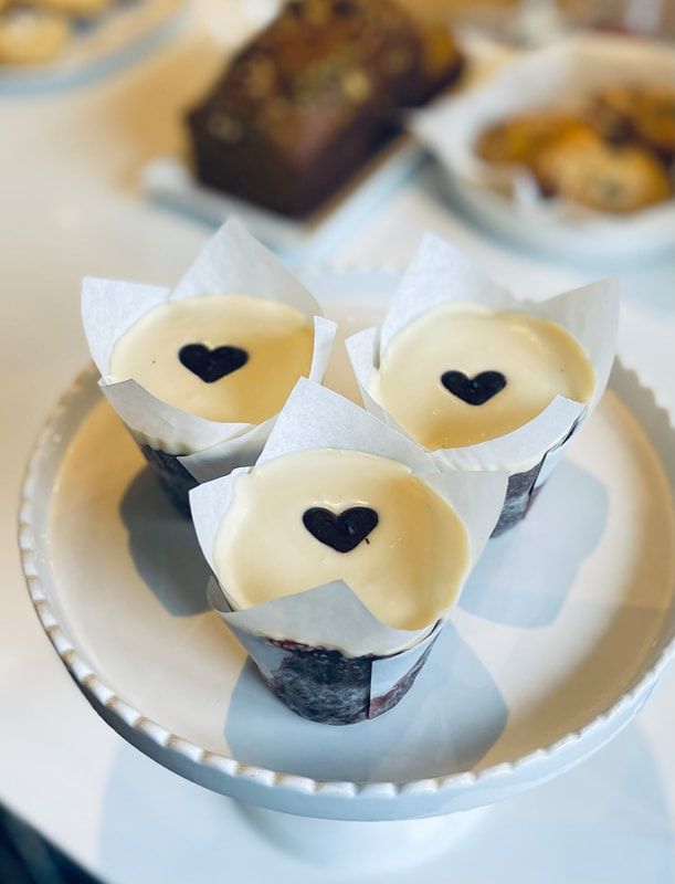 Three white-frosted cupcakes with dark heart decorations on a plate