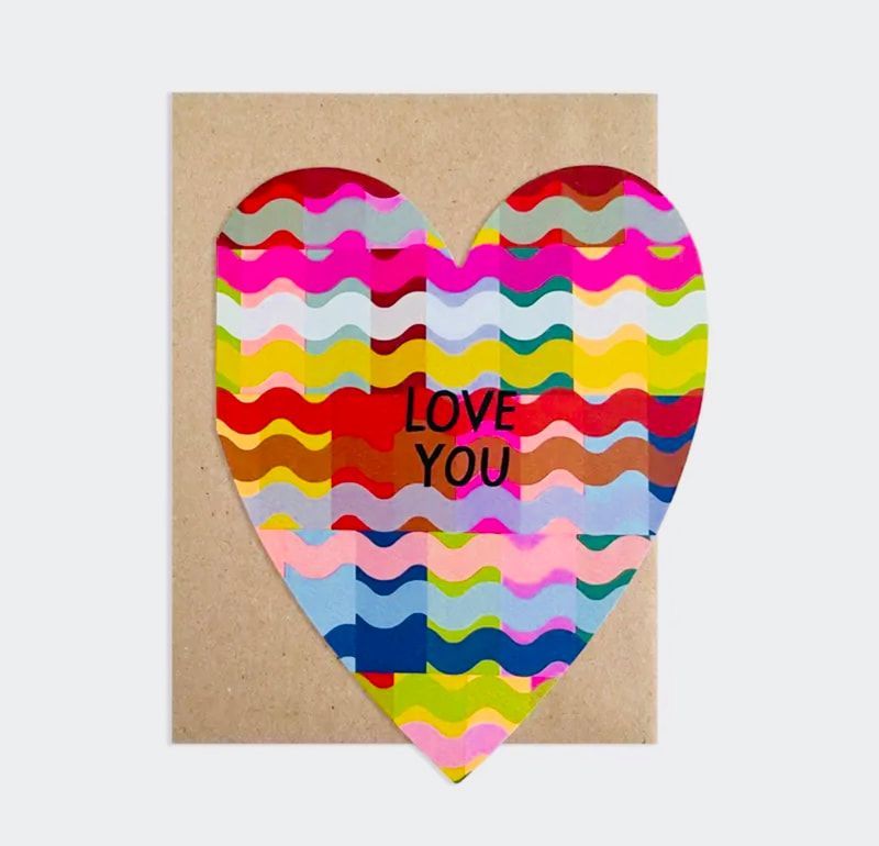 Colorful heart-shaped paper with “LOVE YOU” text on a tan background