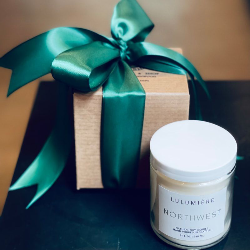 Teal ribbon-tied gift box beside a white jar candle on a dark surface