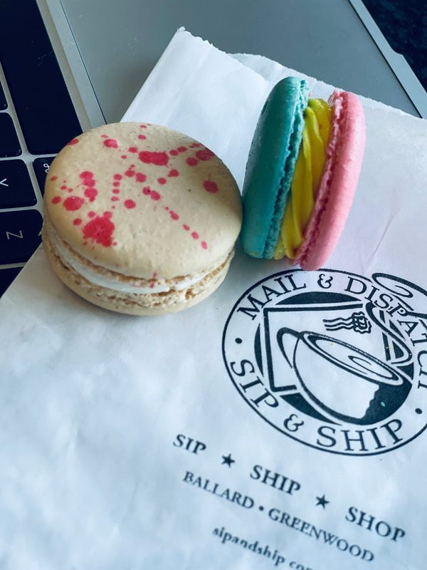 Two colorful macarons on a napkin with a coffee shop logo and laptop nearby