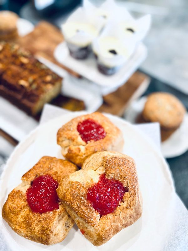 Close-up of strawberry-topped pastries on a white plate with blurred desserts in the background