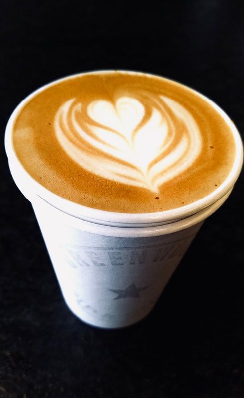 Latte in a white paper cup with heart-shaped latte art on a dark background