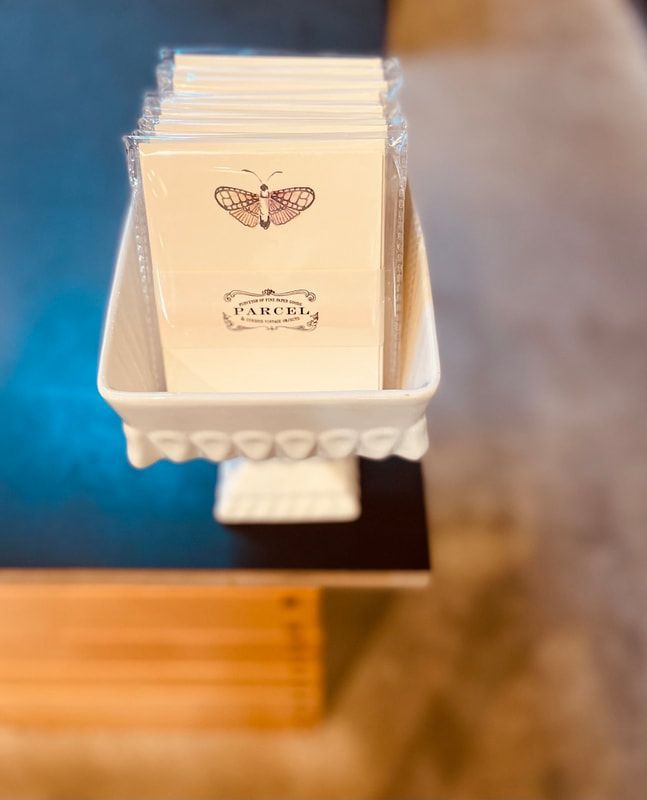 White tray of folded cards with a butterfly logo on a wooden counter.
