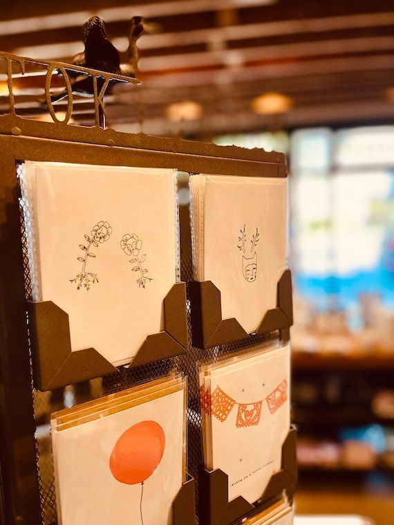 Wooden display rack with beige paper envelopes and cards in a warm indoor shop setting