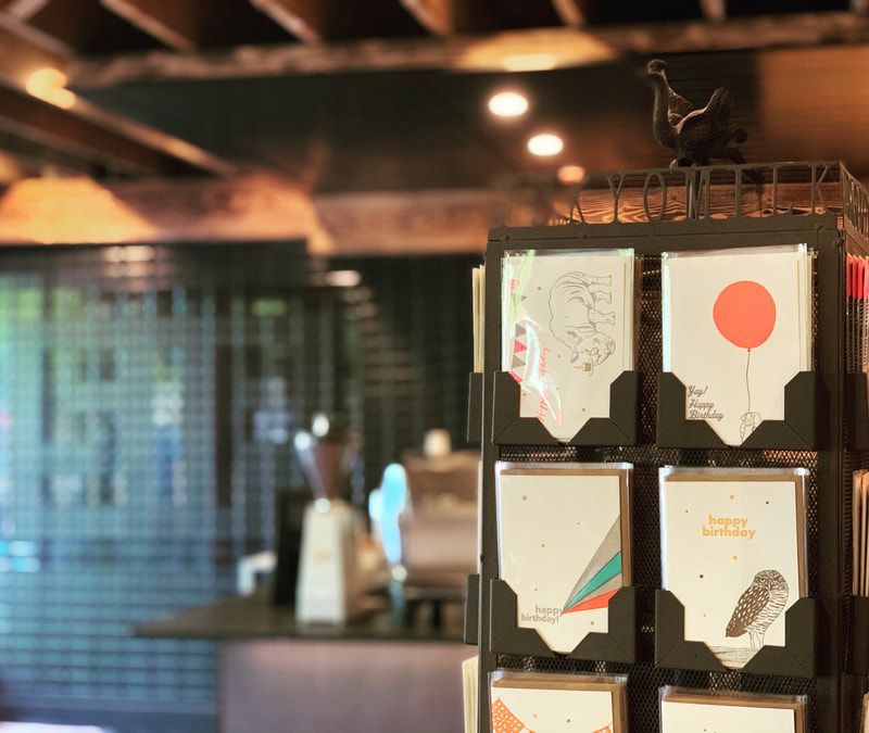 Postcard display rack in a warm-lit shop, with assorted cards and a blurred interior background