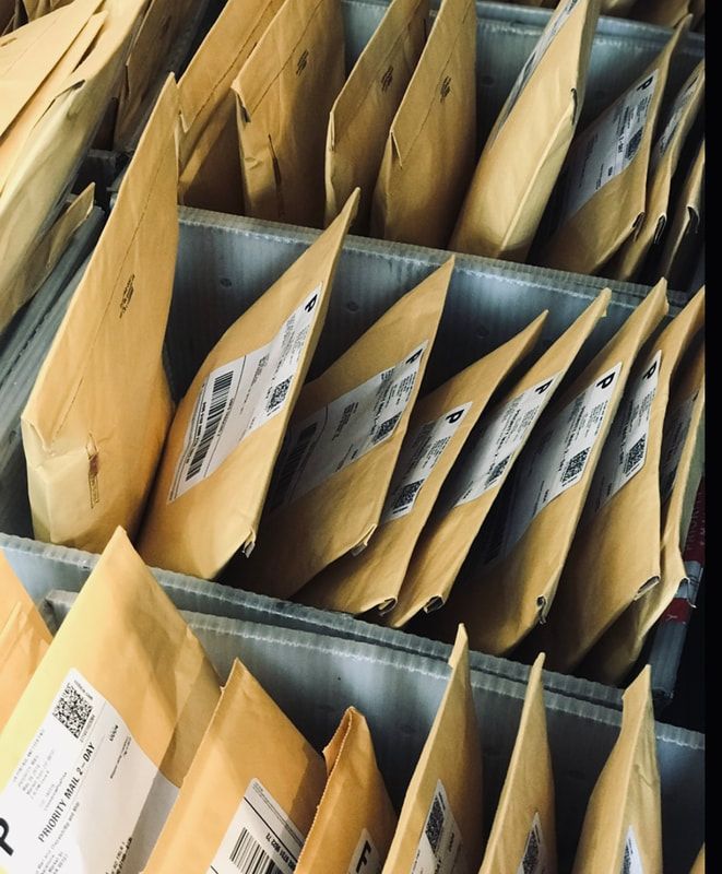 Open cardboard mailers stacked in rows on a metal shelf.