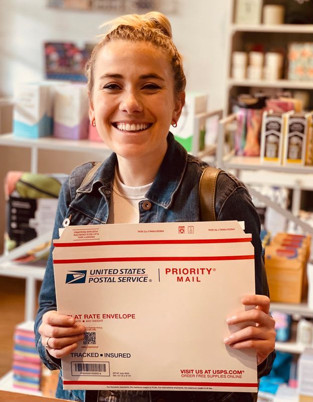 Smiling person holding a USPS Priority Mail envelope in a store aisle