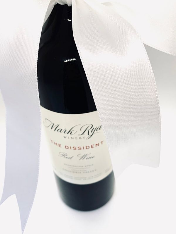 Wine bottle wrapped in white tissue paper with a cream label on a white surface