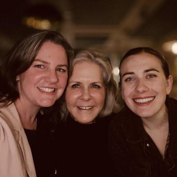 Three smiling people posing closely together in warm indoor lighting.