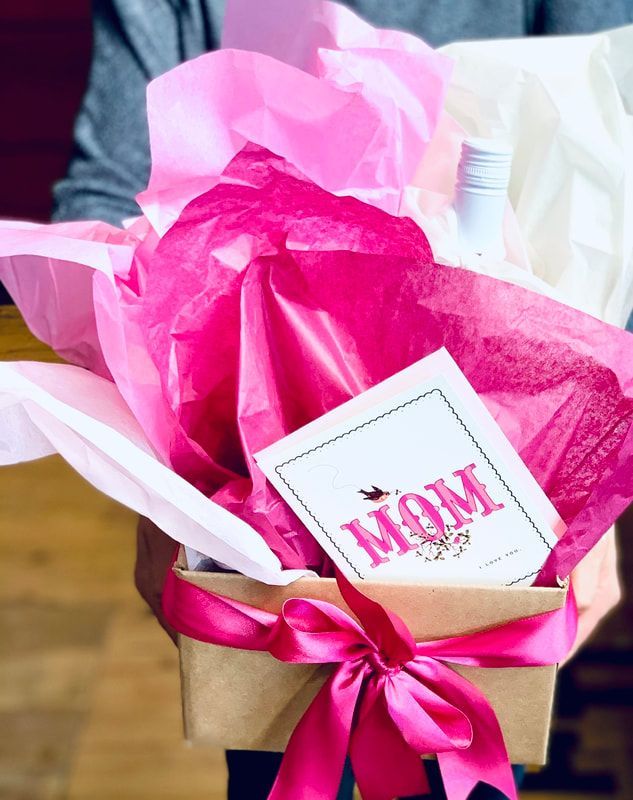 Gift basket with pink tissue paper, a ribbon, and a card reading “Mom”