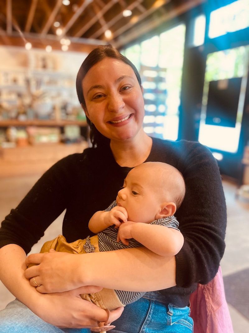 Woman smiling while holding a baby in a bright café or restaurant.