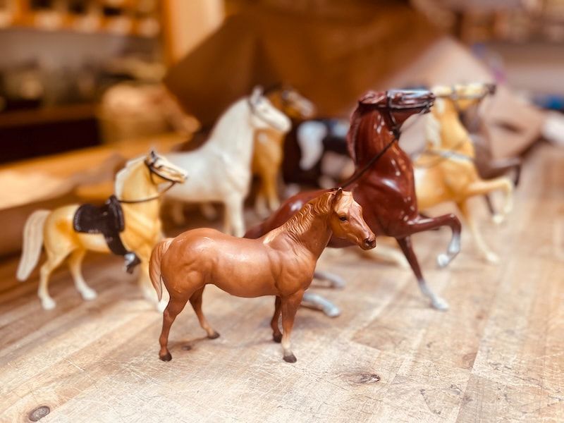 Toy horses arranged on a wooden table, with a brown horse in the foreground and a dark horse behind it