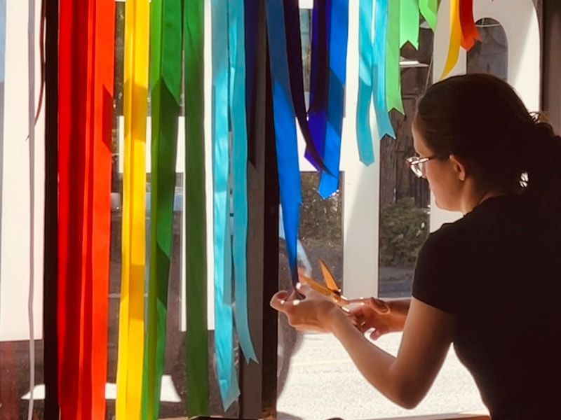 Person arranging colorful hanging ribbons by a bright window