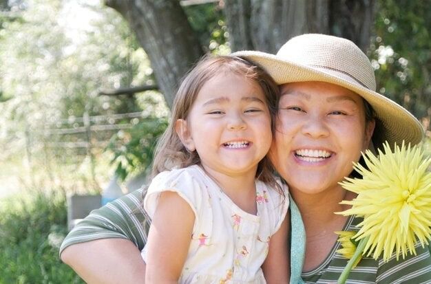 Smiling woman hugging a child outdoors, with a yellow flower in the foreground