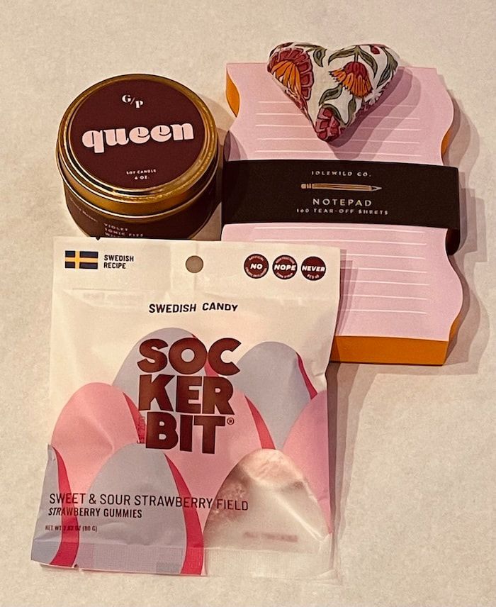 Assorted snack and notebook items on a beige surface, including a Queen tin, socks, and pink notepad
