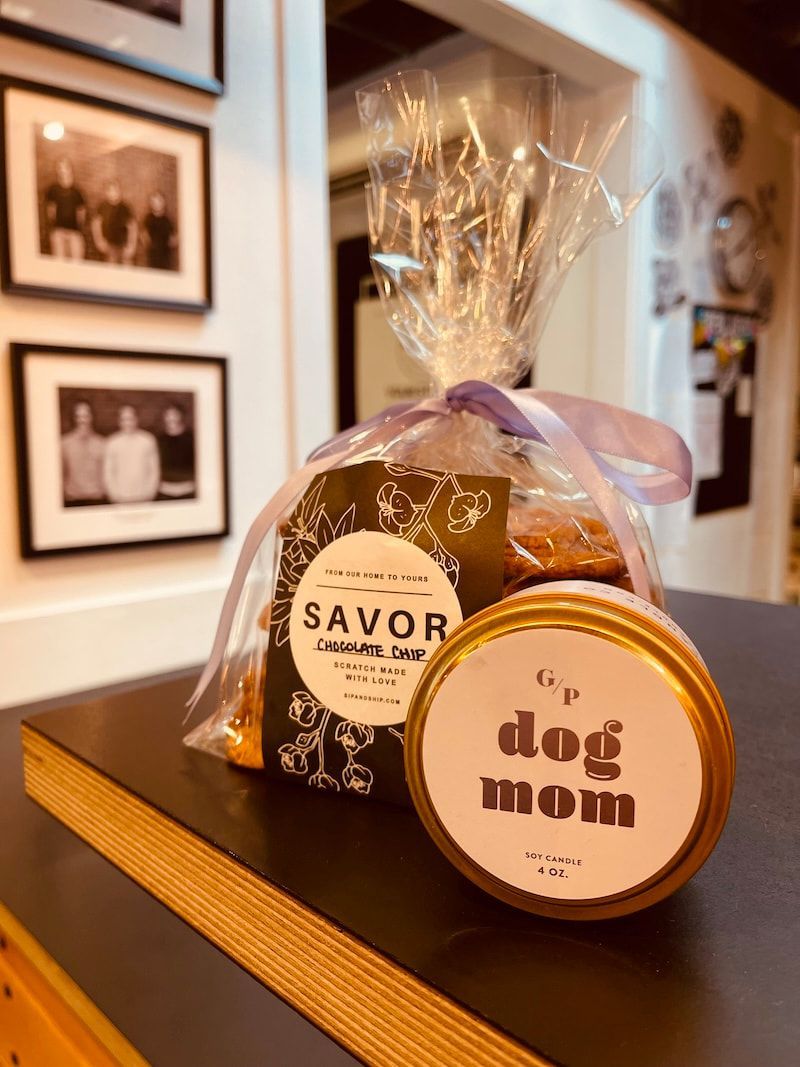 Wrapped dog treats with a “dog mom” tag on a shelf in a framed-photo room
