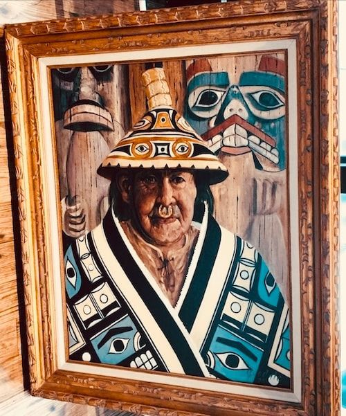 Framed painting of a person in a patterned hat and robe, flanked by stylized carved faces in warm tones