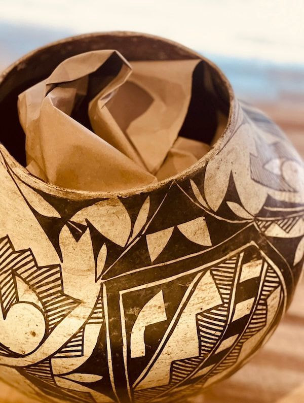 Decorative ceramic vase with black tribal-style patterns, holding crumpled brown paper inside.