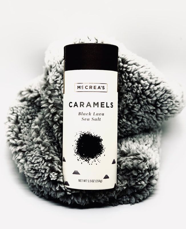 Caramels sea salt candle in white jar with black lid on a fluffy gray blanket
