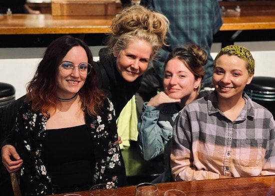 Four people smiling and posing together at a wooden table in a cozy indoor setting