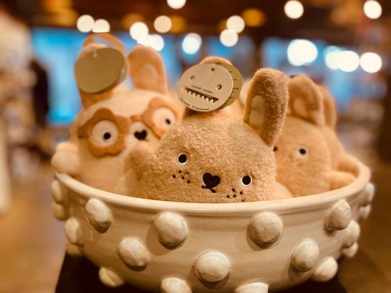 Plush bunny and bear figurines in a white polka-dot bowl, with a warm blurred background.