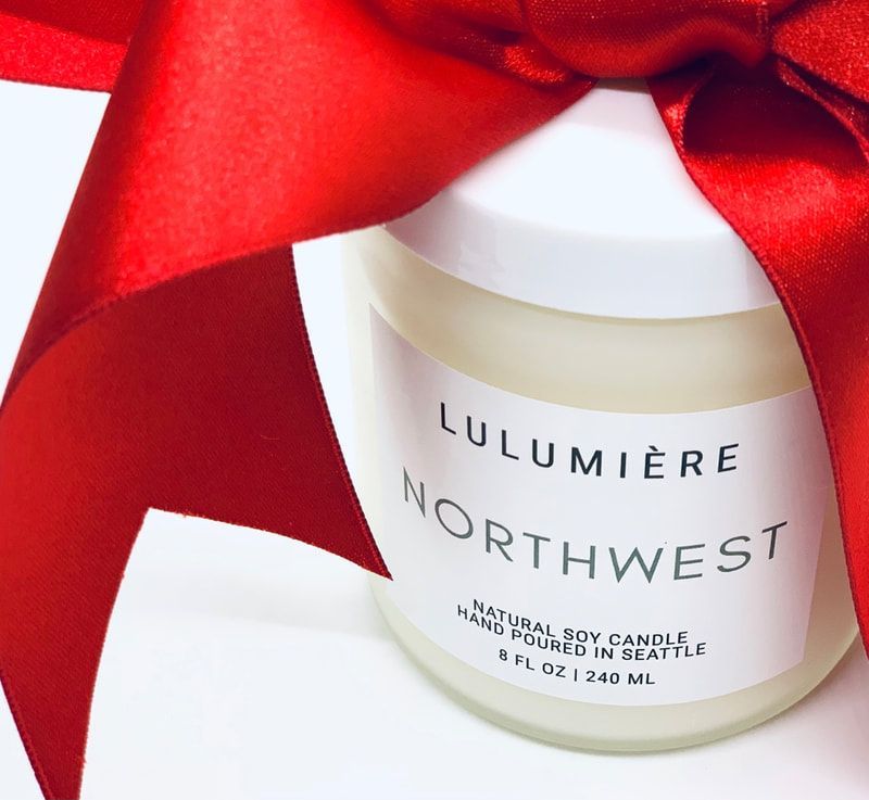 White candle jar with “Lumière Northwest” label wrapped in a red satin ribbon