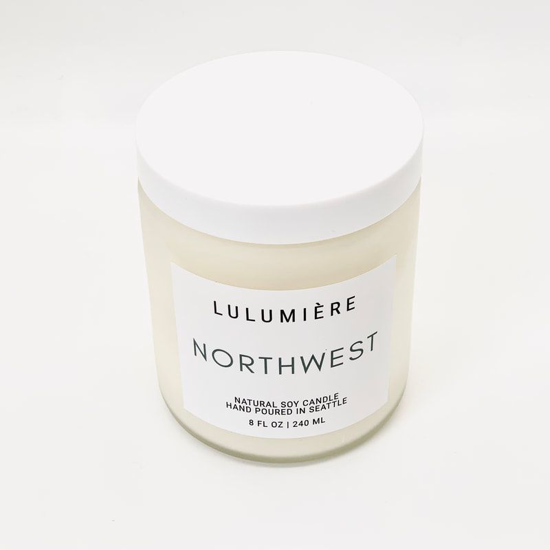 White candle jar labeled “Lulumière Northwest” with a white lid on a plain background