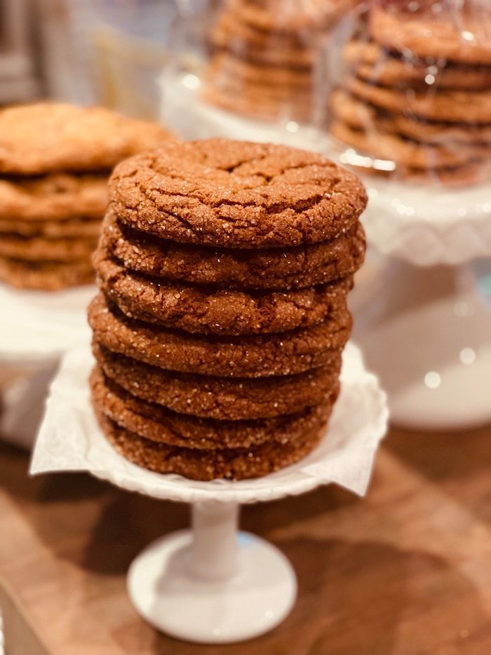 Stack of cinnamon-brown cookies on a white pedestal stand, with more cookies blurred in the background