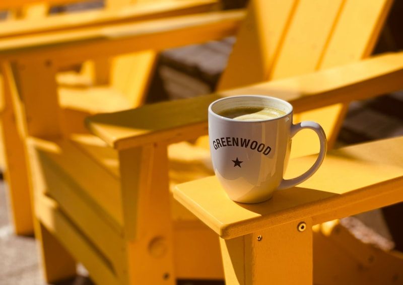White mug on a yellow wooden chair in warm sunlight, with blurred chairs in the background
