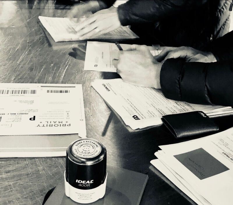 Hands sorting and reading documents on a table beside a small black cylindrical container
