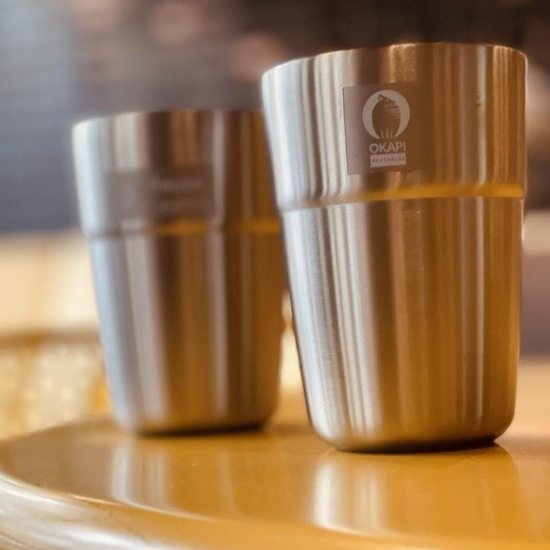 Two stainless steel tumblers on a wooden table, one in sharp focus and one blurred behind it.