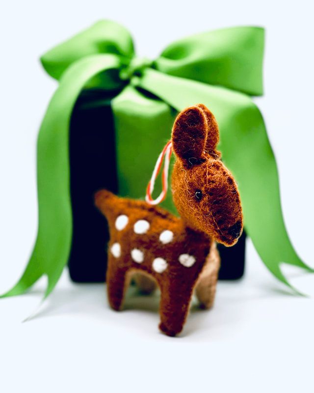 Small plush deer figurine with white spots in front of a green gift box with a ribbon