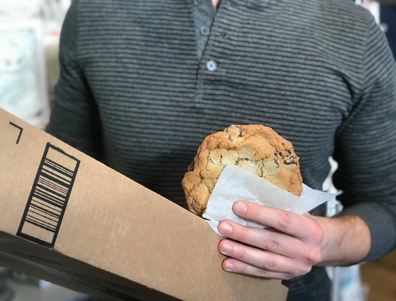 Person holding a large cardboard box and a muffin wrapped in napkin.